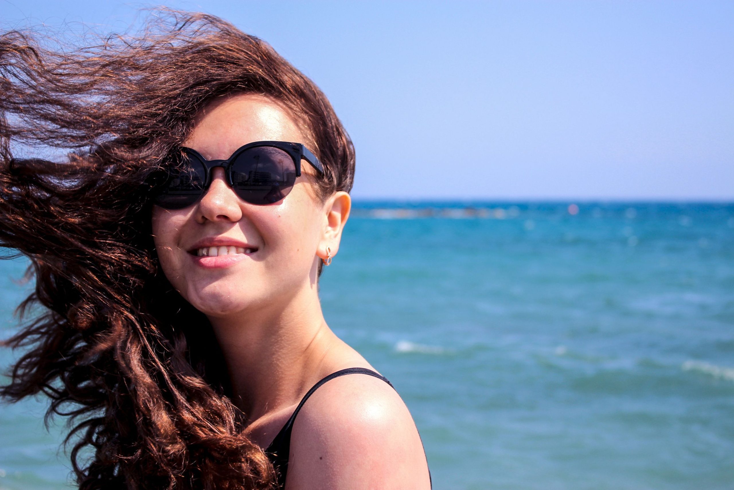 Femme souriante avec lunettes de soleil près de l'océan