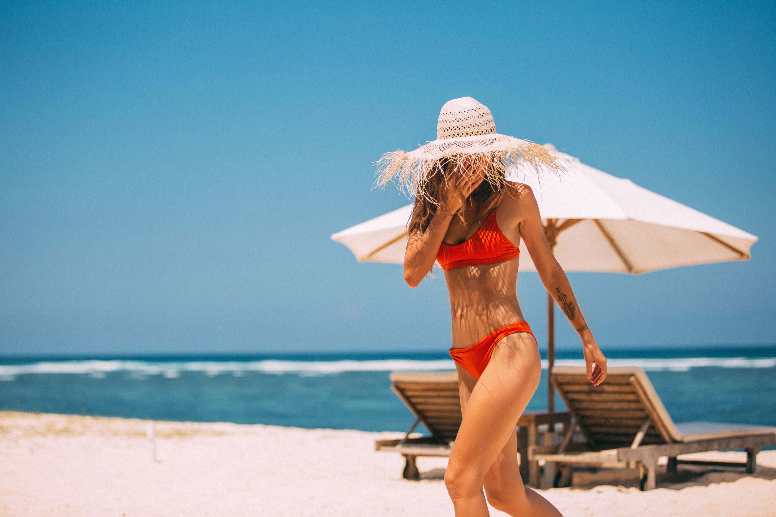 Femme en bikini rouge marchant à la plage avec chapeau